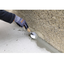 Un artisan applique un mortier de gorge entre le sol et le mur en béton brut à l'aide d'une truelle