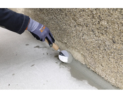 Un artisan applique un mortier de gorge entre le sol et le mur en béton brut à l'aide d'une truelle
