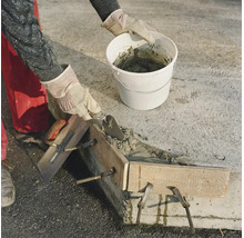 Artisan betonnat un mur avec une truelle et un seau ainsi qu un coffrage en bois sur un chantier.