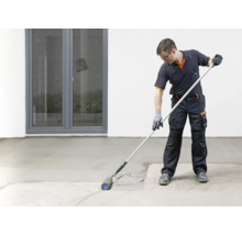 Handwerker in Arbeitskleidung bei der Arbeit mit einer Stachelwalze zum Entlüften von Estrich oder Ausgleichsmasse auf einem Boden.