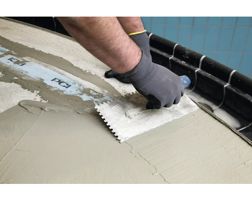 Artisan appliquant de la colle à carrelage avec une taloche crantée sur une bande d etanchéité PCI au sol.