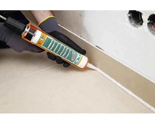 Artisan utilisant un pistolet à cartouche pour appliquer le silicone PCI Silcoferm S sur la plinthe d un mur carrelé