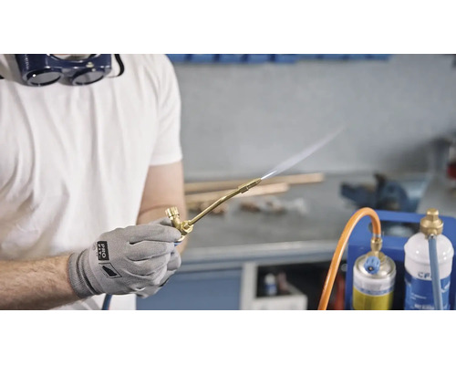 Artisan avec lunettes de protection utilise un chalumeau à gaz dans un atelier.