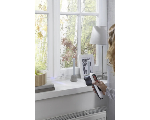 Personne utilisant un détecteur thermique Black et Decker pour vérifier l'isolation des fenêtres dans une pièce lumineuse.