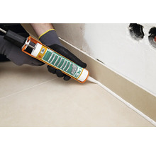 Artisan utilisant un pistolet à cartouche pour appliquer le silicone PCI Silcoferm S sur la plinthe d un mur carrelé