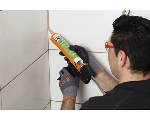Un artisan applique du mastic PCI Silicofug dans le joint de carrelage à l'aide d'un pistolet à cartouche.