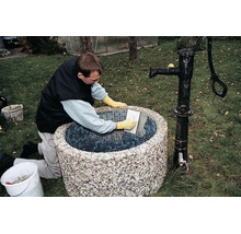 Artisan réalisant le jointoiement d'une fontaine de jardin ronde avec des carreaux de mosaïque.
