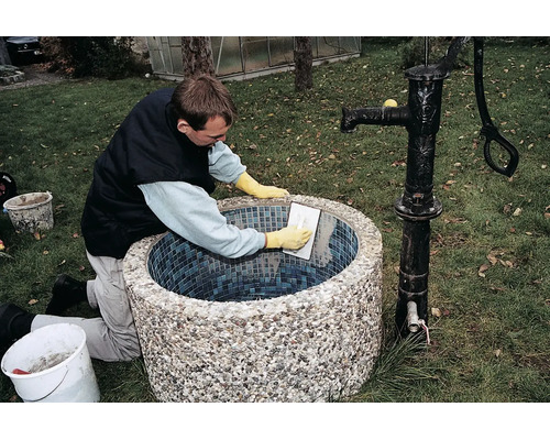 Artisan réalisant le jointoiement d'une fontaine de jardin ronde avec des carreaux de mosaïque.