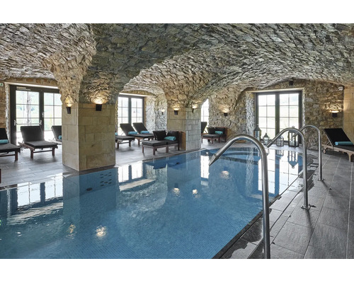 Piscine intérieure située dans une cave voûtée avec des murs en pierre naturelle et des chaises longues dans un espace bien-être.