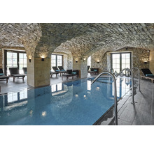 Piscine intérieure située dans une cave voûtée avec des murs en pierre naturelle et des chaises longues dans un espace bien-être.