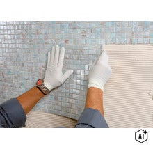 Artisan avec gants posant des carreaux de mosaïque en verre sur une surface murale enduite de colle à carrelage (Image AI modified or generated)