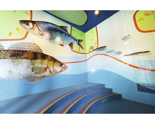 Décoration murale en mosaïque représentant des poissons et escalier incurvé dans un espace intérieur.
