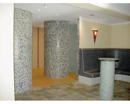 Espace bien-être avec cabines de douche rondes en mosaïque et banc avec surface en mosaïque et éclairage indirect.