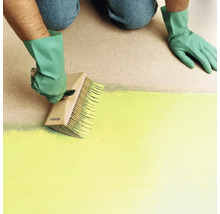 Une personne portant des gants applique de la peinture sur une surface avec une grande brosse à encoller en bois.