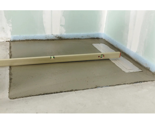 Un niveau à bulle posé sur une chape fraîchement coulée dans une pièce en cours de rénovation.