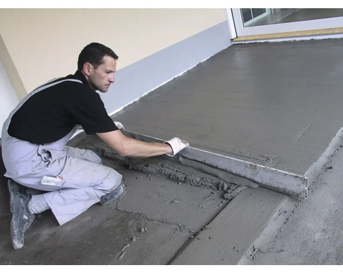 Handwerker glättet frischen Estrichboden auf einer Terrasse mit einer Abziehlatte aus Metall.