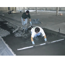 Handwerker bei der professionellen Verlegung von Estrich auf einer grossen Baustelle unter Verwendung einer Abziehlatte.