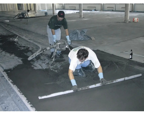 Handwerker bei der professionellen Verlegung von Estrich auf einer grossen Baustelle unter Verwendung einer Abziehlatte.