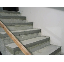 Eine unfertige Betontreppe im Rohbau mit einer hölzernen Führungsschiene an der Seite vor einer glatten Wand.