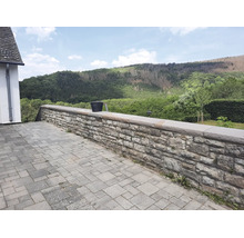 Natursteinmauer aus Bruchsteinen als Terrassenbegrenzung mit Abdeckplatten vor einer bewaldeten Hügellandschaft