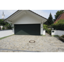 Une allée de garage pavée en pierre naturelle avec un garage blanc et une porte de garage foncée devant une maison.