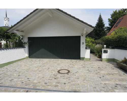 Une allée de garage pavée en pierre naturelle avec un garage blanc et une porte de garage foncée devant une maison.