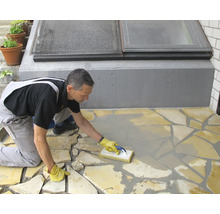 Artisan réalisant le jointoiement d'un revêtement en dalles de pierre naturelle avec une raclette à joints sur une terrasse.