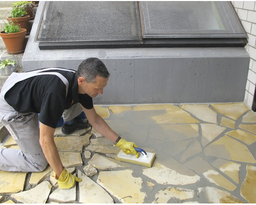 Artisan réalisant le jointoiement d'un revêtement en dalles de pierre naturelle avec une raclette à joints sur une terrasse.