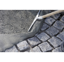 Un ouvrier étale du mortier avec une truelle sur des pavés pour des travaux de pavage.