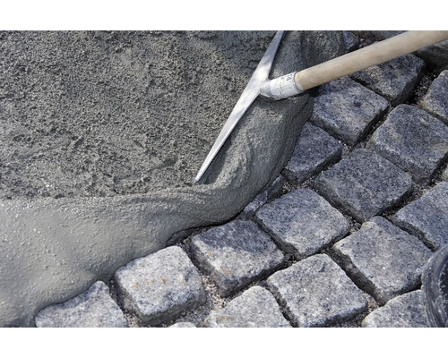 Un ouvrier étale du mortier avec une truelle sur des pavés pour des travaux de pavage.