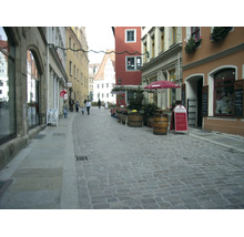 Une ruelle pittoresque de la vieille ville avec des pavés, des bâtiments historiques, des petits magasins et des terrasses avec parasols.