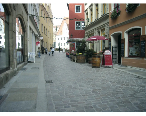 Une ruelle pittoresque de la vieille ville avec des pavés, des bâtiments historiques, des petits magasins et des terrasses avec parasols.