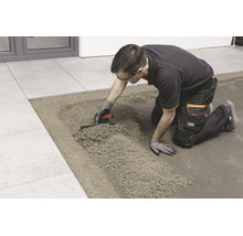 Artisan posant des carreaux sur un lit de mortier de drainage à l'aide d'une truelle.