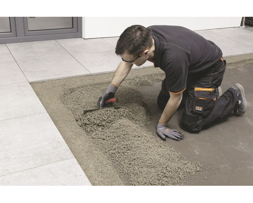 Artisan posant des carreaux sur un lit de mortier de drainage à l'aide d'une truelle.