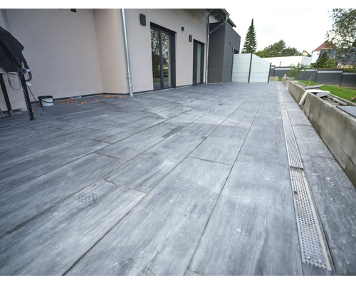 Terrasse avec dalles grand format aspect pierre et caniveau de drainage intégré devant une façade moderne