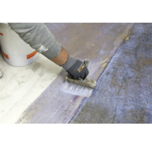 Hand eines Handwerkers beim Auftragen einer Grundierung auf einen Boden mit einem Flächenstreicher.