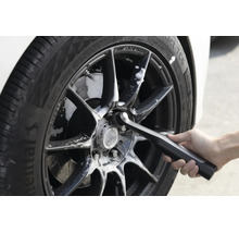 Une personne nettoie une jante de voiture avec une brosse de nettoyage électrique et de la mousse nettoyante.