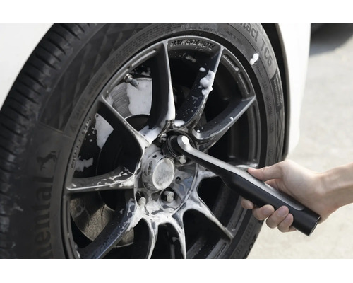 Une personne nettoie une jante de voiture avec une brosse de nettoyage électrique et de la mousse nettoyante.