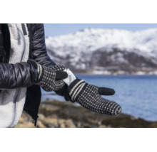 Une personne portant des moufles en tricot insère un chauffe-mains Thermopad dans son gant devant un paysage hivernal avec montagne et lac.