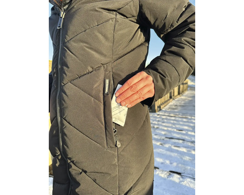 Une personne porte une veste d hiver matelassée et insère un coussin chauffant Thermopad dans la poche zippée.