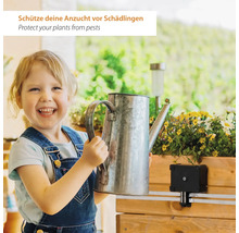 Un enfant joyeux tient un arrosoir à côté d'une jardinière en bois équipée d'un dispositif de protection contre les nuisibles.