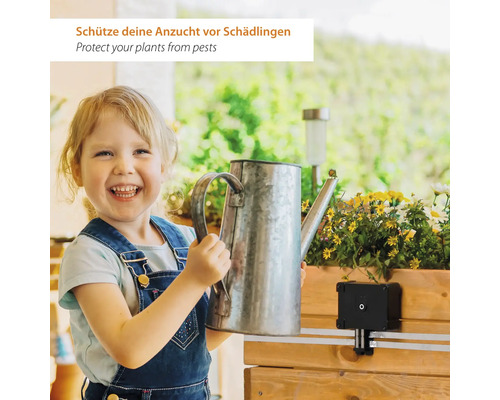 Un enfant joyeux tient un arrosoir à côté d'une jardinière en bois équipée d'un dispositif de protection contre les nuisibles.