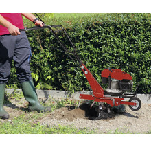 Une personne utilise une motobineuse thermique dans un jardin devant une haie.