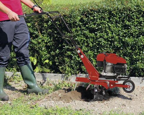 Une personne utilise une motobineuse thermique dans un jardin devant une haie.