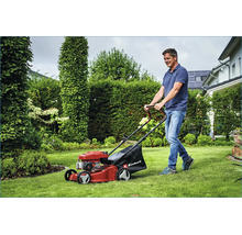 Ein Mann mäht den Rasen mit einem Benzin Rasenmäher von Einhell in einem grünen Garten.