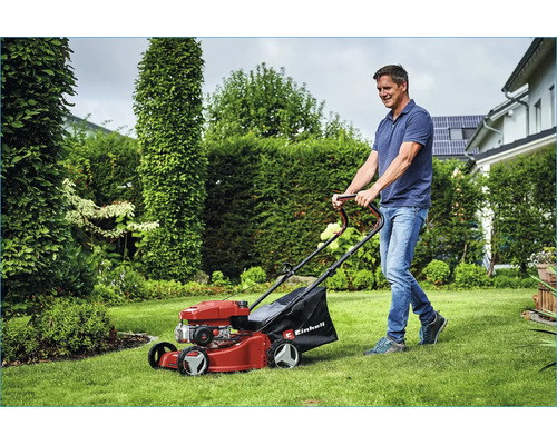 Ein Mann mäht den Rasen mit einem Benzin Rasenmäher von Einhell in einem grünen Garten.