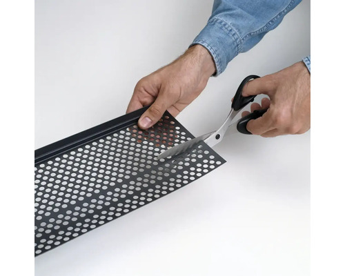 Eine Person schneidet mit einer Haushaltsschere ein perforiertes Blech aus Metall zurecht.