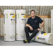 Homme en tenue de travail assis dans des combles isolés avec des rouleaux d'isolant Isover Lanae de conductivité thermique 031.