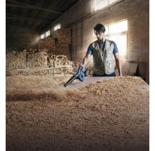 Un artisan utilise un souffleur sans fil Bosch pour nettoyer des copeaux de bois sur une pièce dans un atelier.