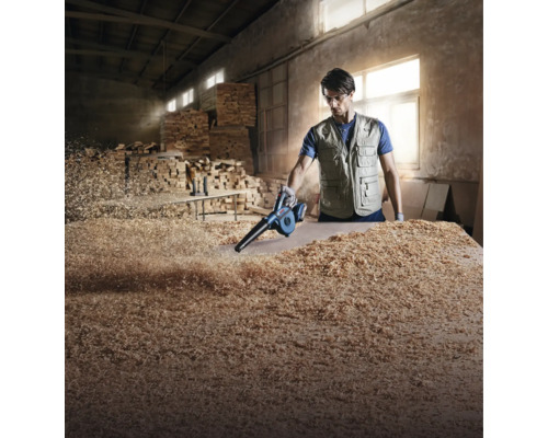 Un artisan utilise un souffleur sans fil Bosch pour nettoyer des copeaux de bois sur une pièce dans un atelier.